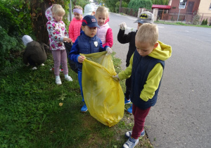 chłopcy trzymają żółty worek na śmieci a 4 dzieci zbiera papierki